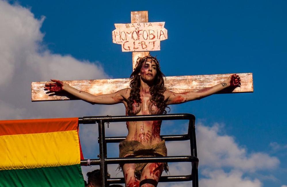 Una joven simula la crucifixión bajo el cartel 'basta de homofobia'