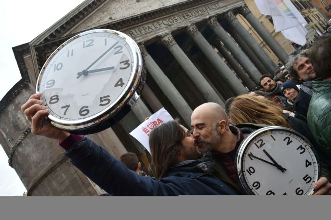Dos manifestantes se besan en Roma sujetando dos relojes para simbolizar que Italia está atrasada respecto a otros países